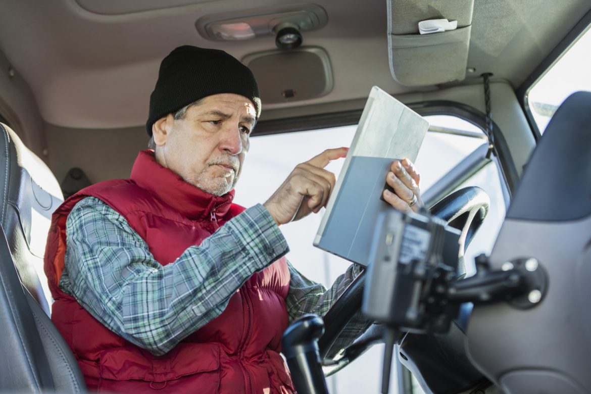 Senior Hispanic man driving semi-truck, using tablet